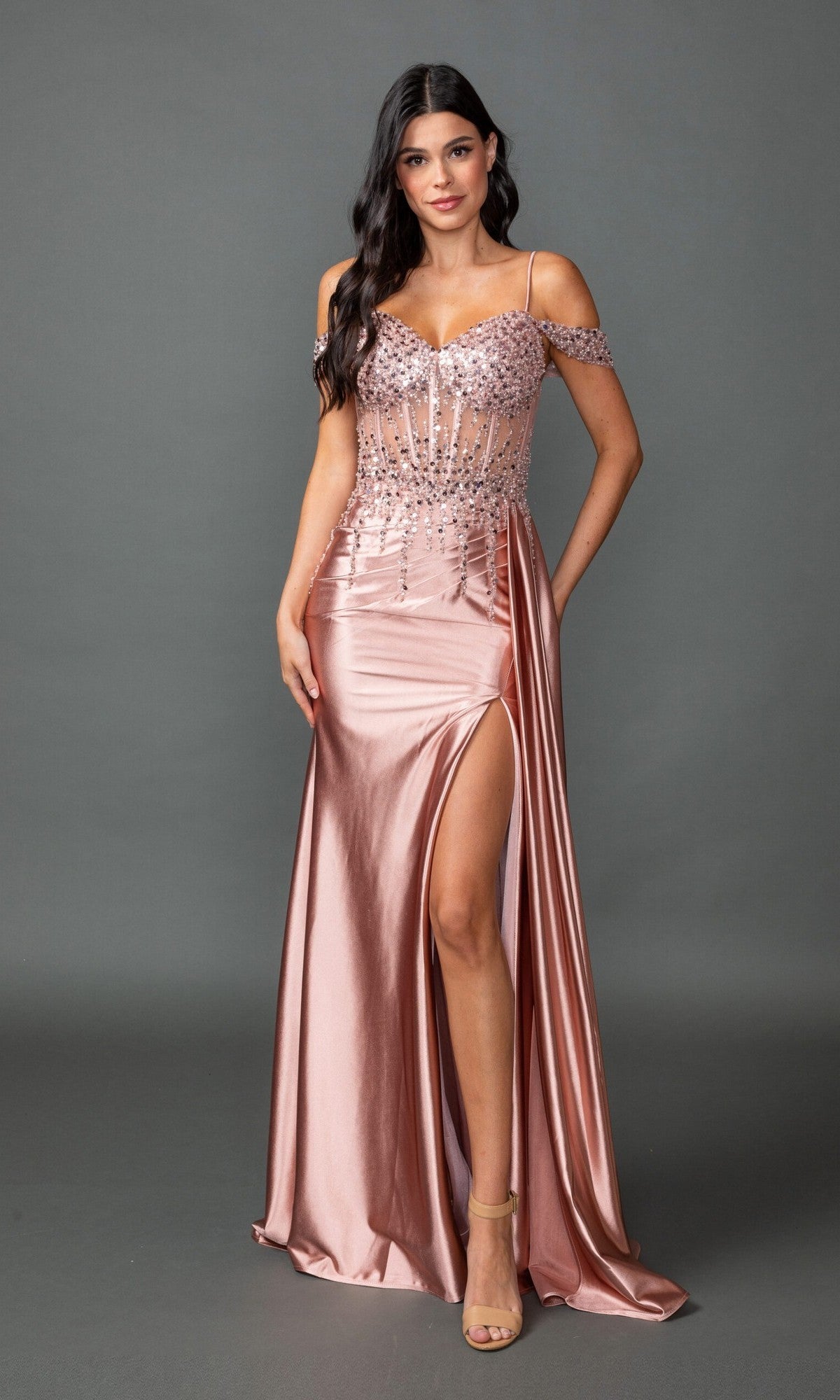 A woman poses against a gray background wearing the Dancing Queen 4551 long prom dress in rose gold, featuring sequin embellishments, off-the-shoulder straps, and a high leg slit.